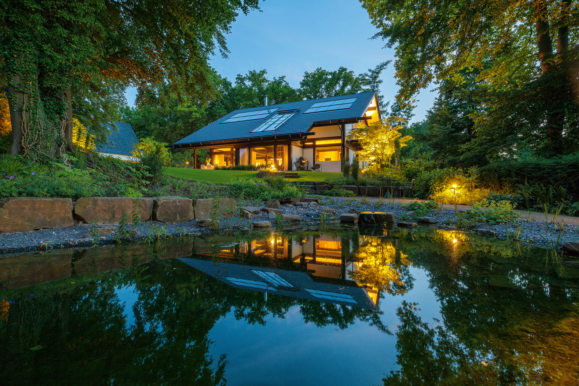 Architektenhaus mit Garten und Reflexion im Wasser bei Sonnenuntergang