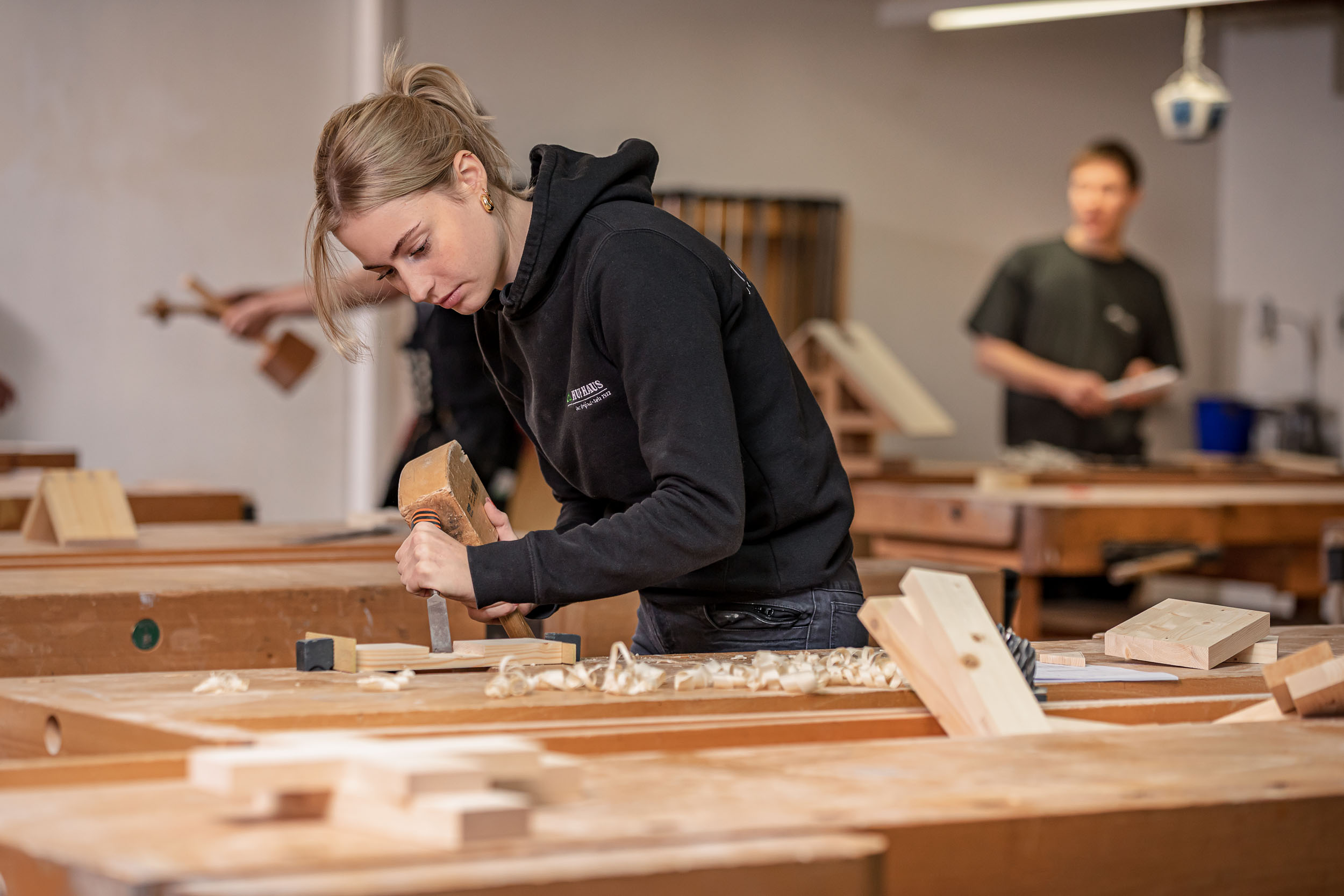 Junge Frau beim Holzarbeiten in einer Werkstatt Eine Frau arbeitet konzentriert mit einem Meißel an Holz in einer Tischlerei