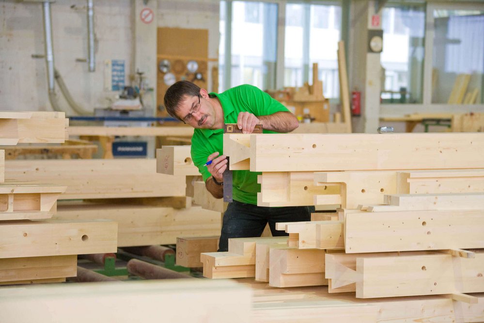Holzschutz bei HUF HAUS Handwerker prüft Holzstücke in einer Holzwerkstatt