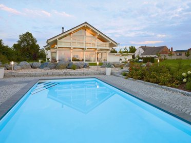 Fachwerkhaus HUF HAUS ART 4 mit Pool Moderne Architektur mit Pool und Gartenanlage im Hintergrund