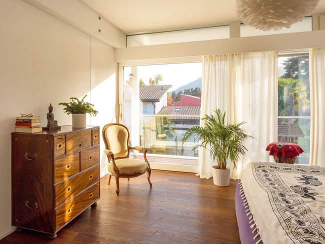 Helles Schlafzimmer mit Pflanzen, Holzkommode und Fensterblick