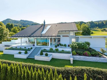 Modernes Haus mit Aussicht auf Hügel und See, umgeben von Garten.