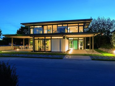Moderne Villa bei Nacht mit Garten und Außenbeleuchtung Schöne moderne Architektur einer Villa umgeben von grünen Bäumen