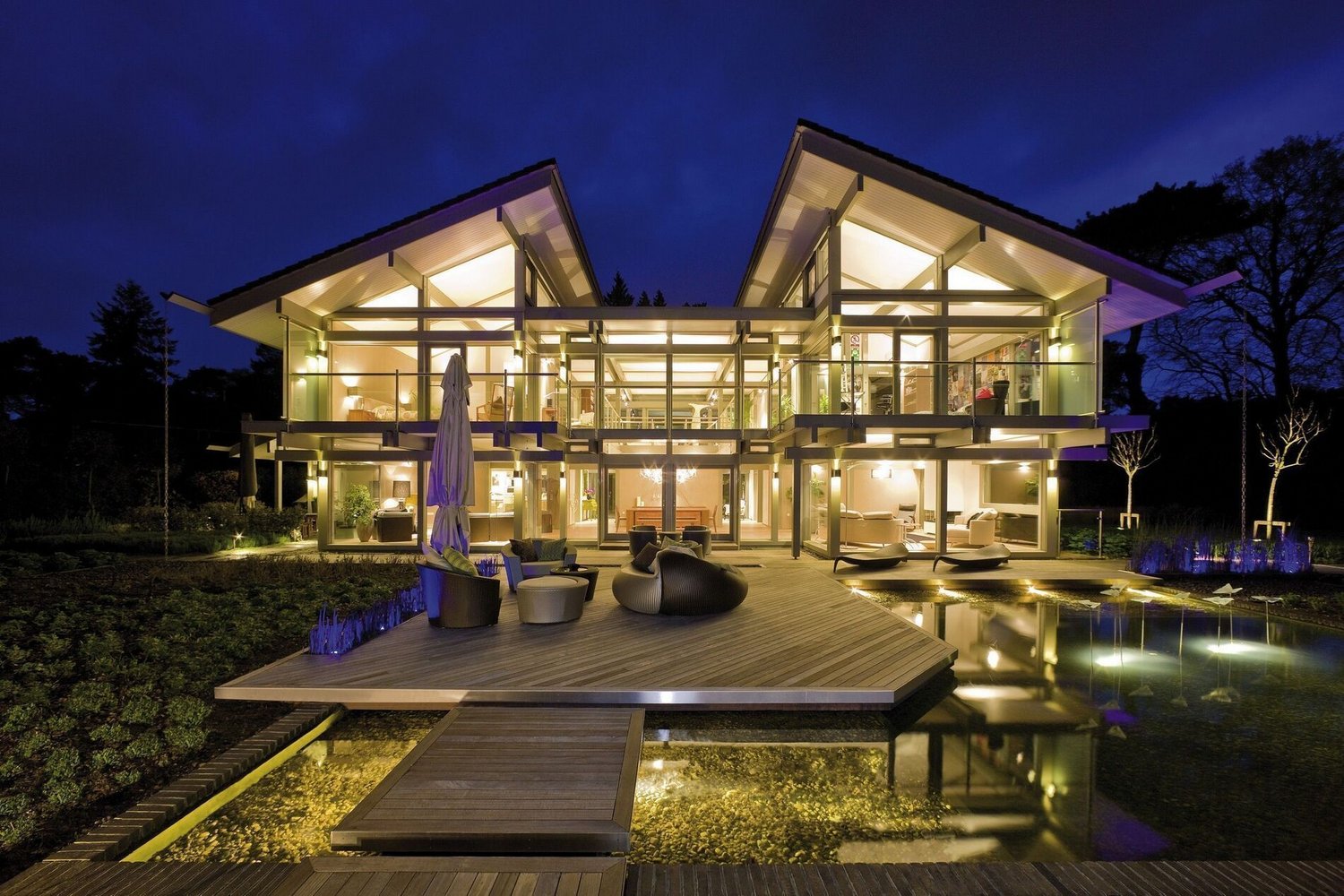 Helles modernes Haus mit großzügigem Garten und Wasserfläche bei Nacht