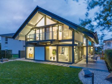 Moderne Architektur eines Einfamilienhauses bei Dämmerung Einfamilienhaus mit Glasfassade und Garten bei Nachtbeleuchtung