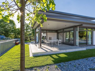 Moderne Architektur eines Wohnhauses mit Terrasse Geräumige Terrasse mit Garten und moderner Bauweise