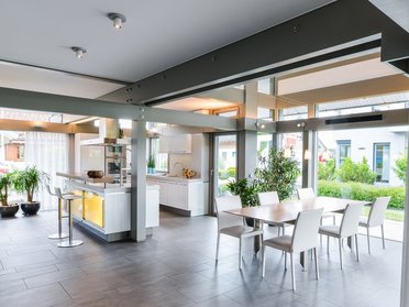 Helle, offene Küche mit Esstisch und Pflanzen im Hintergrund