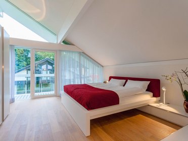 Helles Schlafzimmer mit Schrägdach, Balkon und minimalistischer Einrichtung