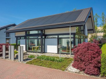 Modernes Einfamilienhaus mit Garten und Auffahrt Helles Haus mit großen Fenstern, umgeben von buntem Garten