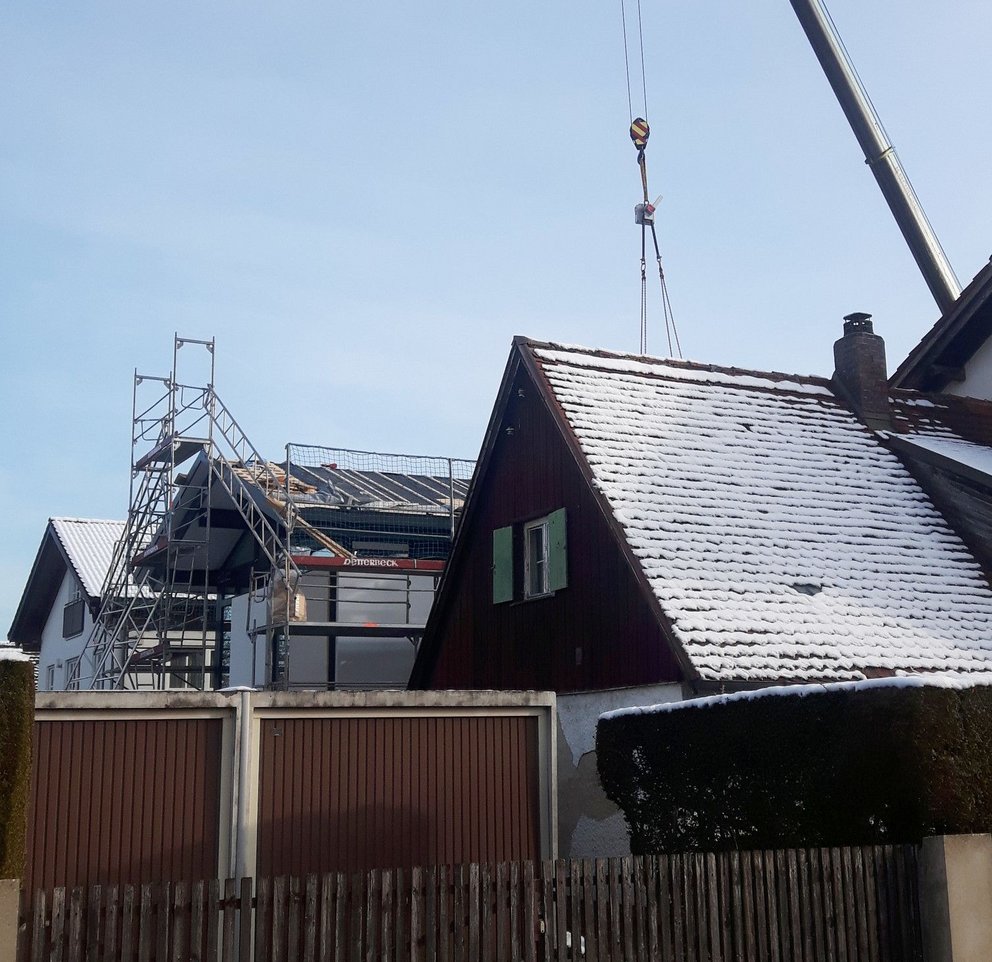 Bauarbeiten mit Kran an einem Wohnhaus Kran hebt Material auf ein Dach eines mit Schnee bedeckten Hauses