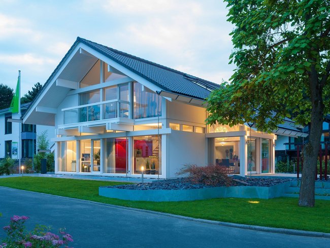 Ein modernes Haus mit großen Fenstern und einem gepflegten Garten bei Dämmerung