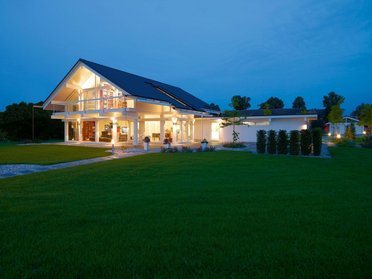Fachwerkhaus HUF HAUS ART 4 bei Nacht Ein modernes Fachwerkhaus mit großer Glasfront und Gartenbeleuchtung