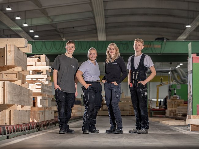 Gruppe junger Handwerker in einer Holzwerkstatt Vier Personen in Arbeitskleidung stehen in einer Holzwerkstatt