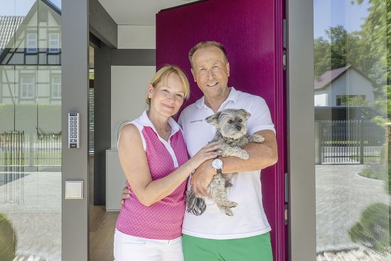Paar steht vor dem Eingang eines modernen Hauses mit Hund