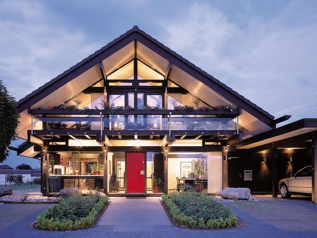 Moderne Architektur eines Hauses bei Dämmerung Ansicht eines modernen Hauses mit Glasfront und roter Tür bei Nacht
