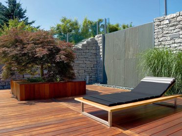 Elegante Liege auf einer Holzterrasse mit bepflanzten Akzenten