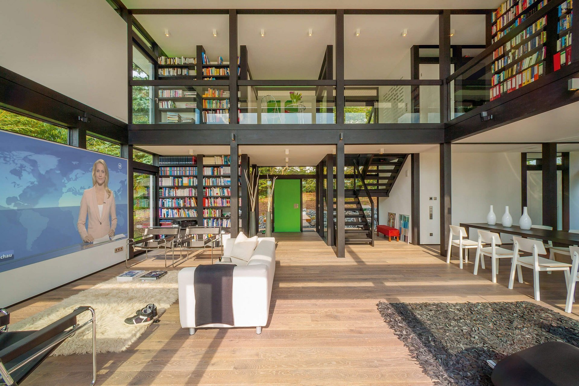Modernes Wohnzimmer mit Büchern und Fernseher Helles, modernes Wohnzimmer mit großer Fensterfront und Bibliothek