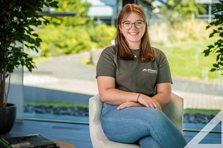 Junge Frau sitzt in einem modernen Raum Eine junge Frau in einem grauen T-Shirt sitzt lächelnd in einem hellen Innenraum
