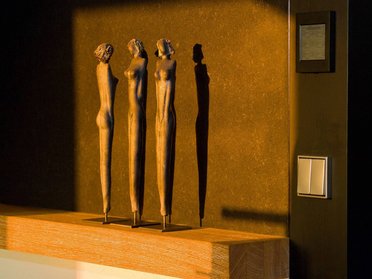 Drei stilisierte Skulpturen werfen Schatten auf eine Wand