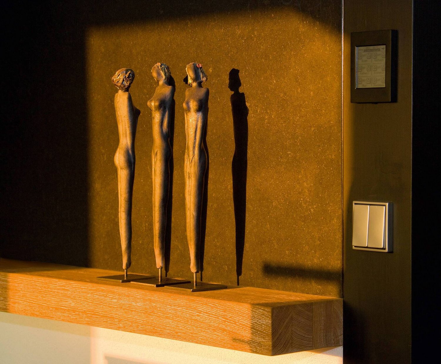 Drei stilisierte Skulpturen werfen Schatten auf eine Wand