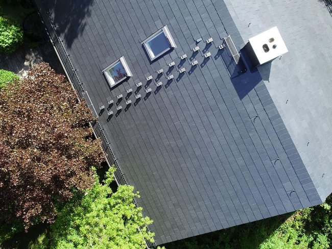 Moderne Architektur mit schwarzem Dach und Grünflächen Luftaufnahme eines Dachüberstands mit umliegenden Bäumen und Sträuchern