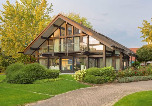 Elegantes Haus mit Balkon, umgeben von grünem Garten und Bäumen
