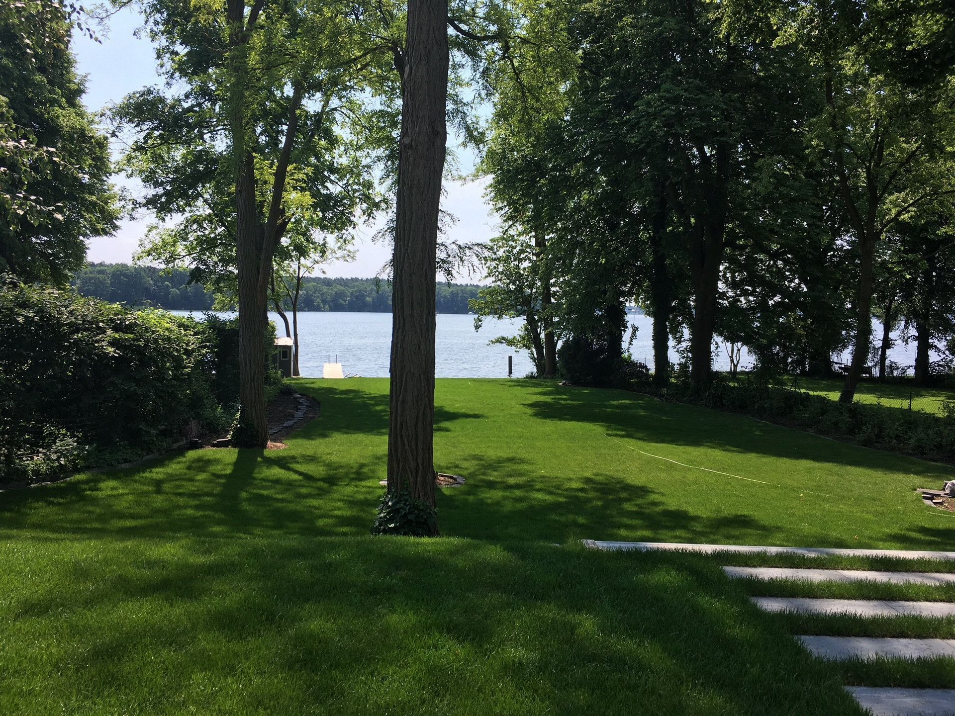 Grünes Ufer mit Blick auf den See Überblick über eine grüne Rasenfläche am See, umgeben von Bäumen.