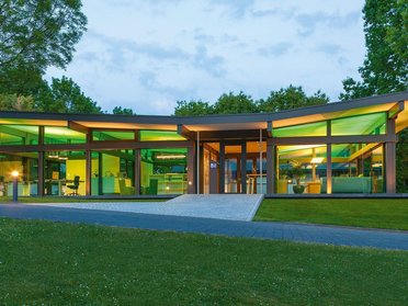 Moderne Architektur mit grüner Beleuchtung Zeitgenössisches Gebäude mit großen Fenstern und Gartenlandschaft