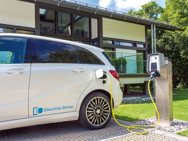 Ein Elektroauto wird an einer Ladestation vor einem modernen Haus aufgeladen.