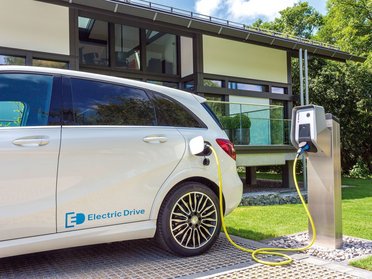Ein Elektroauto wird an einer Ladestation vor einem modernen Haus aufgeladen.