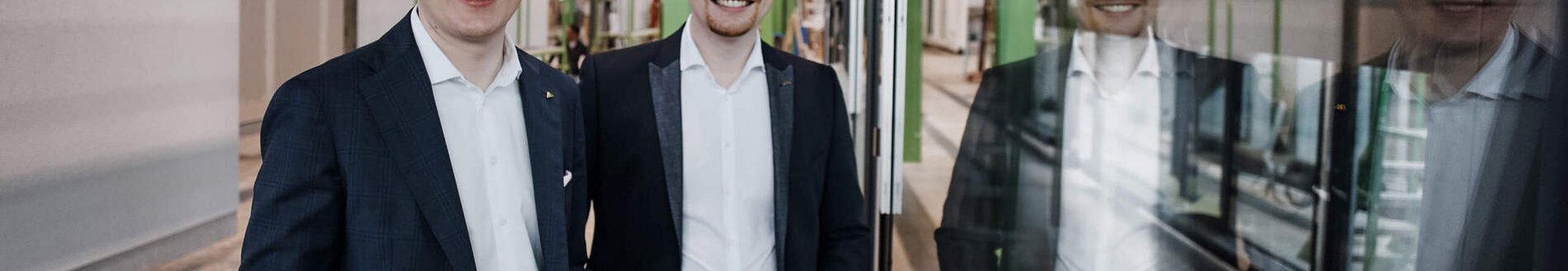 Zwei Männer in moderner Industrieumgebung Zwei Männer posieren vor einem gläsernen Element in einer Fabrikhalle