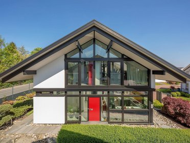 Moderne Architektur mit großflächigen Fenstern und Garten Haus mit gewinkeltem Dach, großen Fenstern und gepflegtem Garten