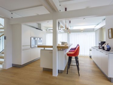 Elegante, helle Küche mit weißen Schränken und Barstühlen