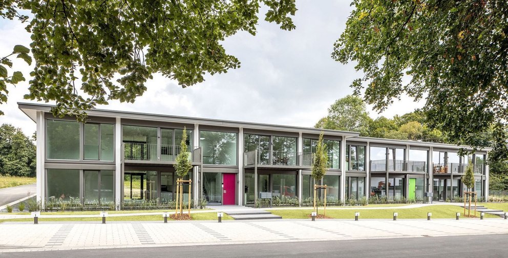 Ein modernes Gebäude mit großen Fenstern und bunten Türen in einer ruhigen Umgebung.