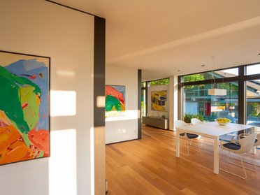 Helles Wohnzimmer mit großen Fenstern, modernen Möbeln und bunten Gemälden