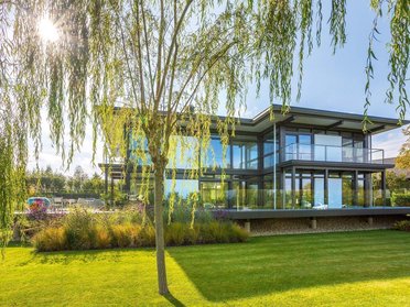 Modernes Flachdachhaus umgeben von grünem Rasen und Weidenbaum