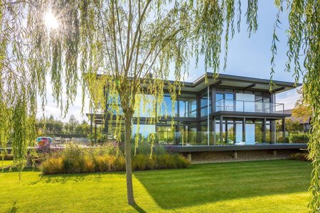 Luxushaus mit Flachdach in sonniger Gartenlandschaft Modernes Flachdachhaus umgeben von grünem Rasen und Weidenbaum
