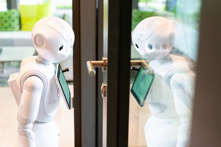 A robot with a tablet stands at a glass door.