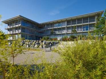 Moderne Architektur des Bürogebäudes HUF mit Pflanzen und Steinmauer im Vordergrund