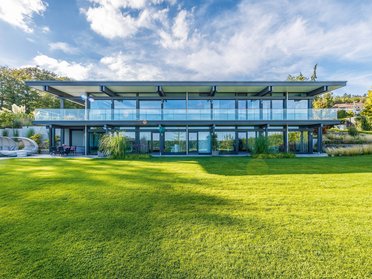 Moderne Architektur des HUF HAUS mit großzügigen Glasfronten und grünem Garten