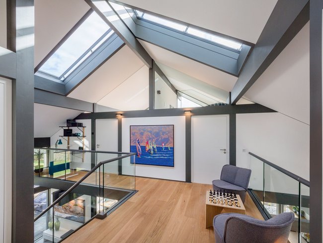 Modernes Wohnzimmer mit Dachschrägen und Kunstwerk Helle offene Wohnfläche mit Glasgeländer und Kunstwerk an der Wand