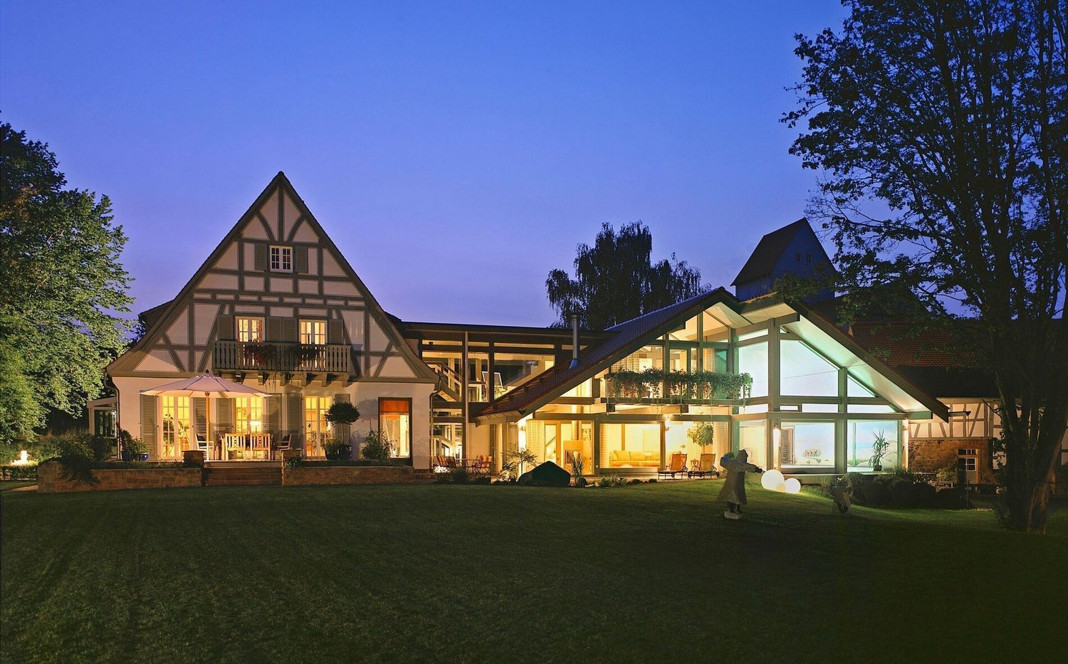 Abendansicht eines Hauses mit unterschiedlichen Anbauten und Garten