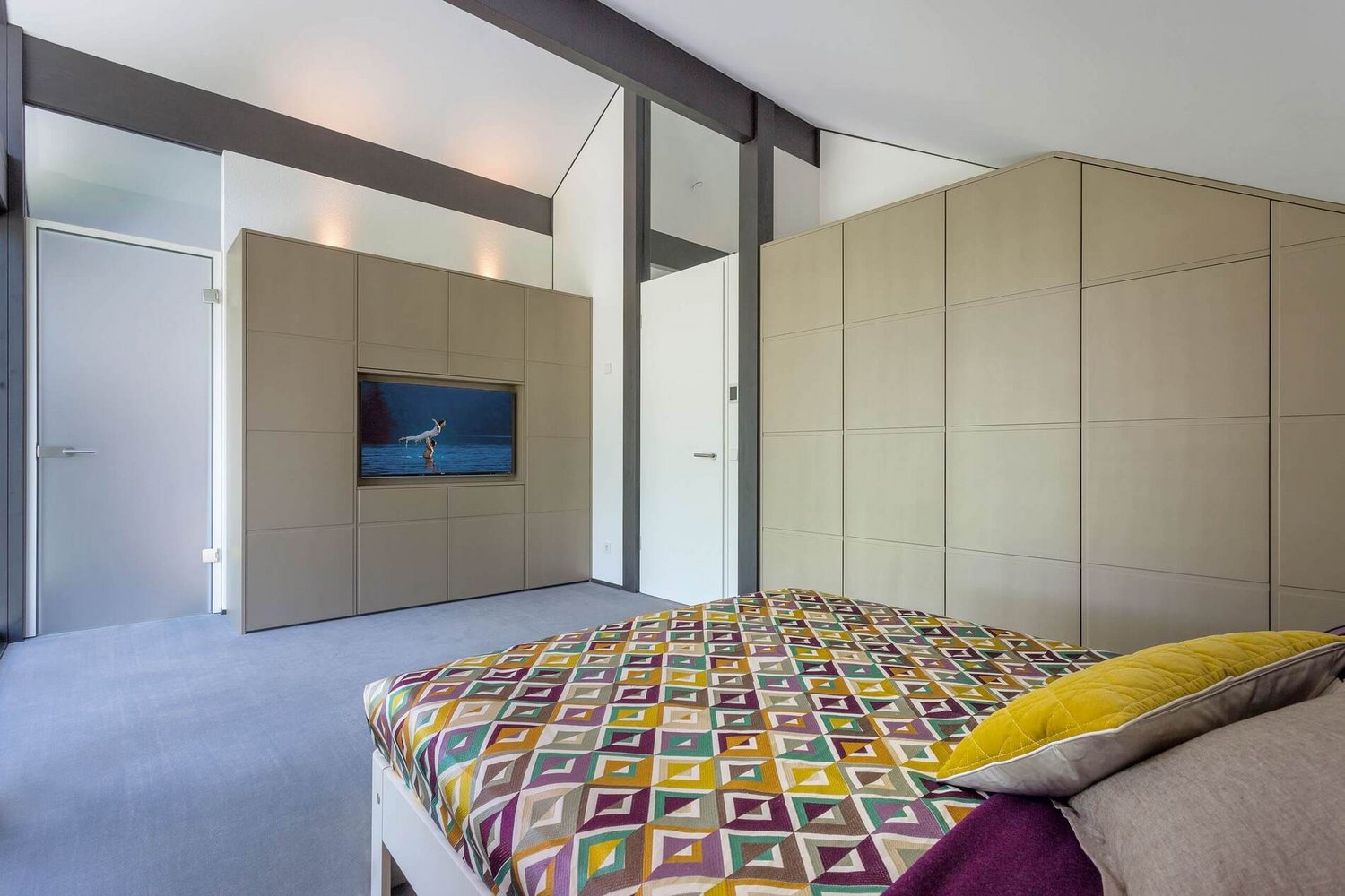 Helles Schlafzimmer mit TV und geometrischem Bettüberwurf