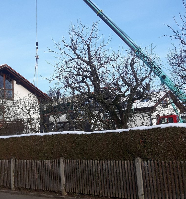 Großer Kran hebt Last über einen Zaun in einem Wohngebiet