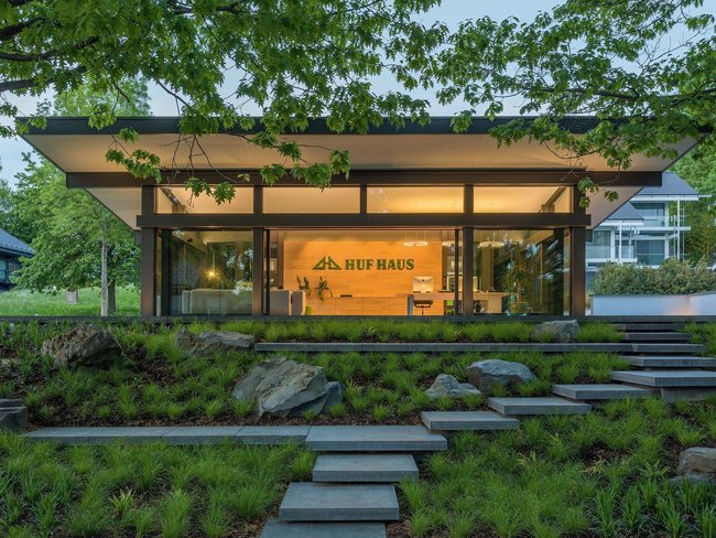 Moderne Architektur von HUF HAUS in grüner Umgebung HUF HAUS mit Glasfassade und begrüntem Gelände im Vordergrund