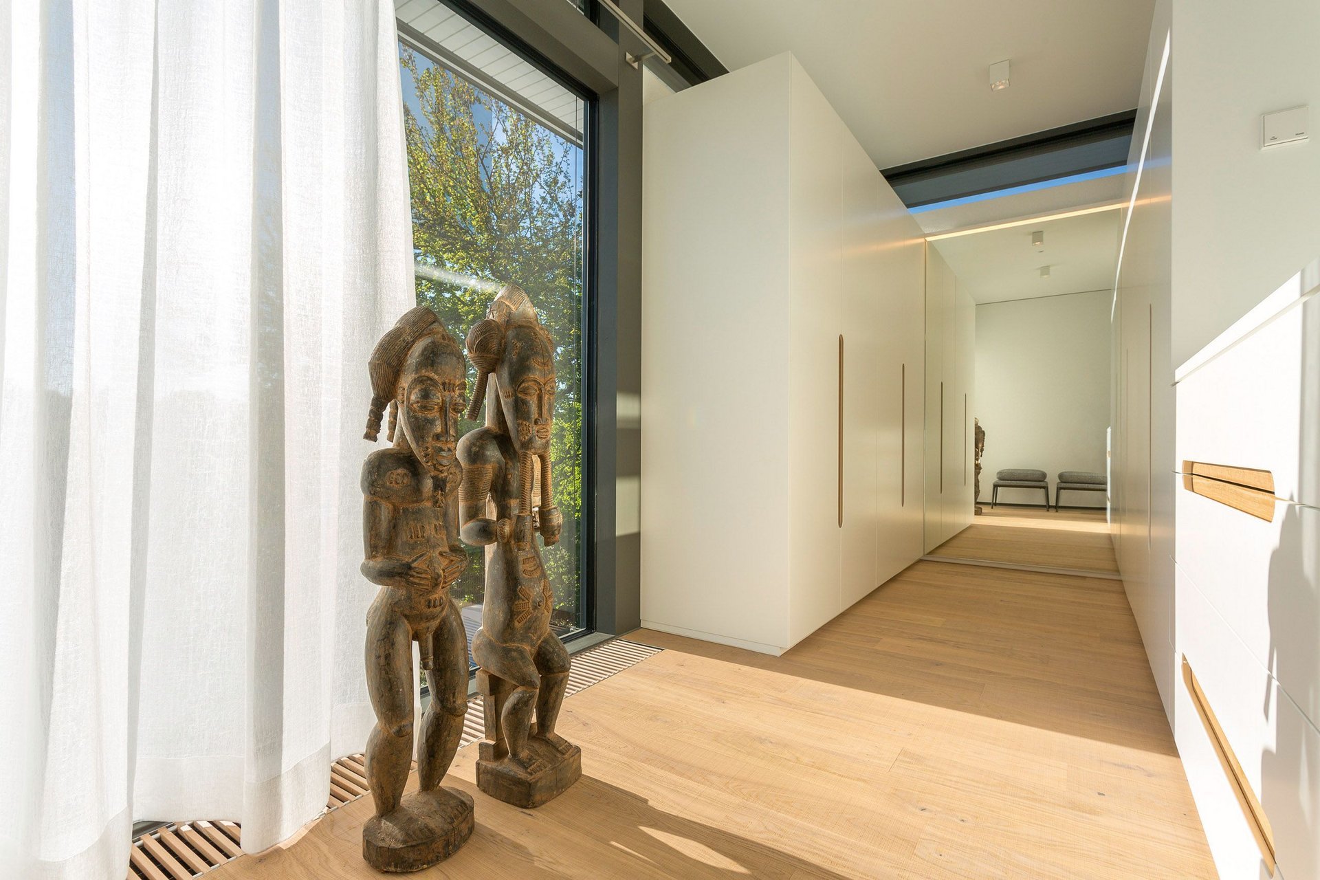 Bright hallway featuring decorative wooden sculptures and large windows