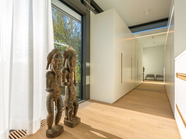 Modern hallway with wooden flooring and sculptures Bright hallway featuring decorative wooden sculptures and large windows