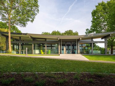 Moderne Architektur eines Gebäudes in einer Parklandschaft Ansicht eines modernen Gebäudes umgeben von Bäumen und Rasenflächen