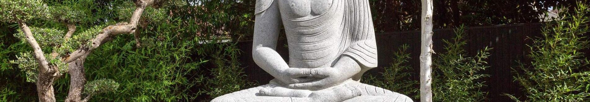 Graue Buddha-Statue im Garten mit Pflanzen und Kies