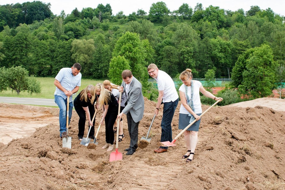 Gruppenfoto bei der Grundsteinlegung mit Schaufeln auf Sand.